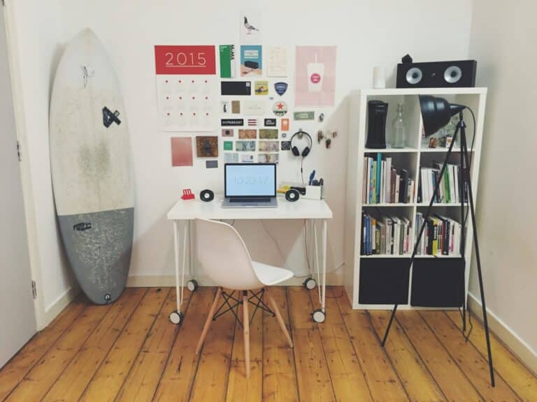 White surfboard beside white wall white wooden cube bookshelf inside the room